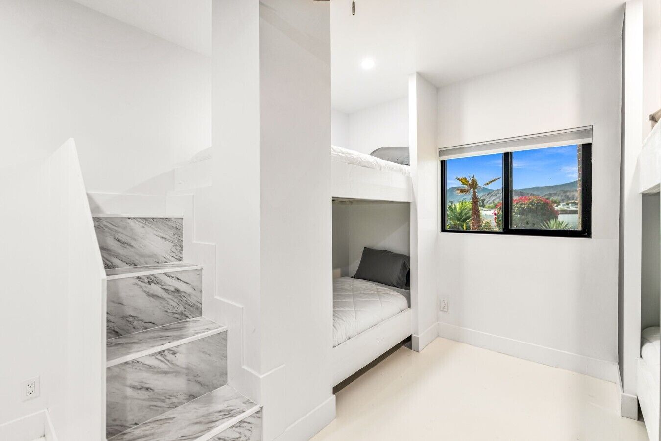 Ein kleiner Raum mit Etagenbett, einer Marmortreppe und einem Fenster mit Blick ins Grüne.