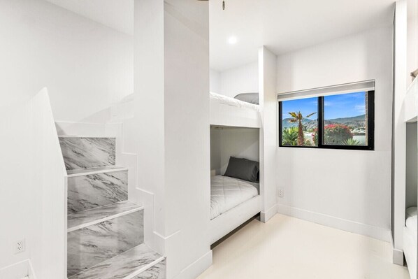 A compact room with a bunk bed, a marble staircase, and a window with a view of greenery.