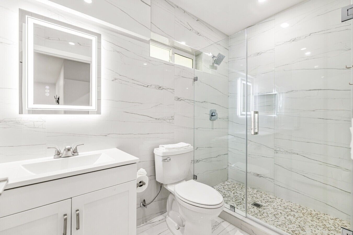 Un bagno moderno con un lavabo in marmo bianco, un water e una cabina doccia in vetro.
