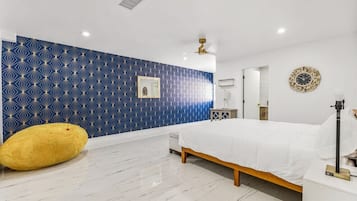 A bedroom with a bed, a yellow bean bag, a mirror, a clock, and a ceiling fan.