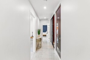 A hallway with white walls, a marble floor, and a round table with a plant.