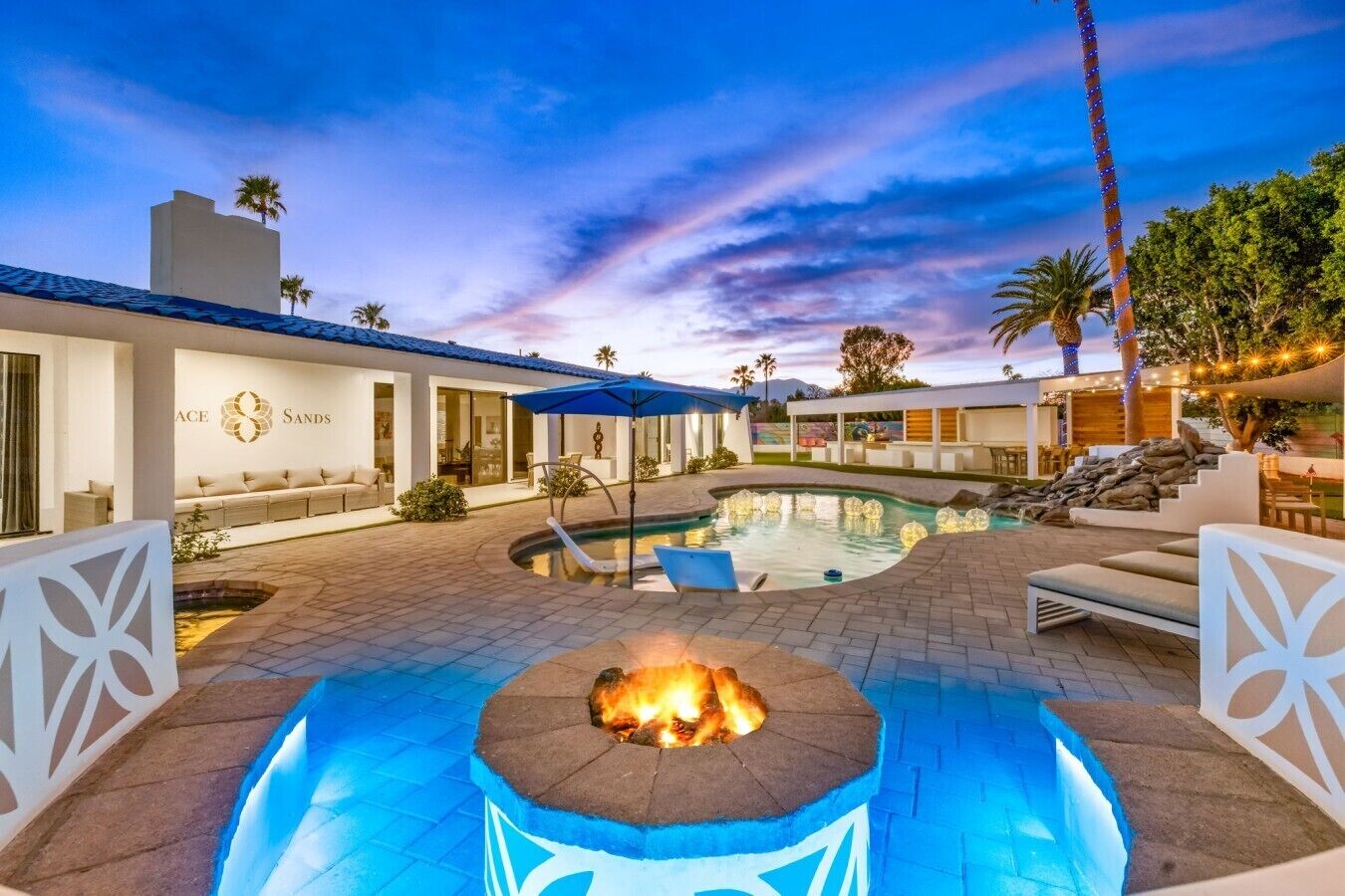 A modern outdoor pool area with a fire pit, lounge seating, and a clear sky.