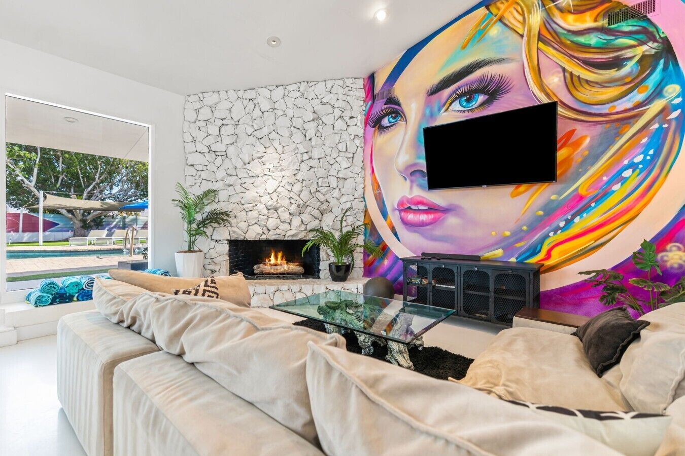Ein modernes Wohnzimmer mit Kamin aus Stein, einem großen Fernseher und einem farbenfrohen Wandbild.