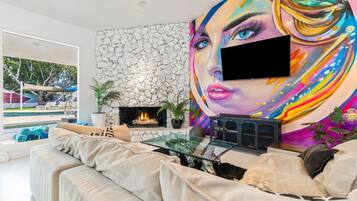 Una sala de estar moderna con chimenea de piedra, un televisor grande y un mural colorido.