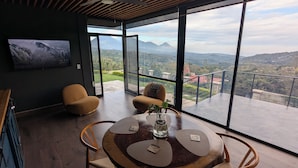 A modern interior with a dining table, chairs, and a large window offering a mountain view. - 1 bedroom guesthouse with volcano views throughout the home in Juayua (Juayua)