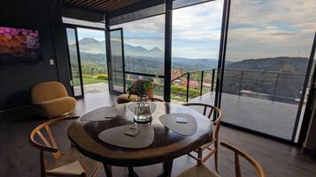 Un espace de restauration moderne comprenant une table, des chaises et une vue sur les montagnes, visible à travers de grandes fenêtres.