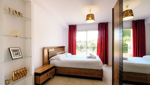 Een moderne hotelkamer met een houten bed, een nachtkastje, een glazen plank met decoratieve objecten en een grote spiegel.