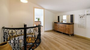 Een ruime kamer met een houten vloer, een zwart ijzeren balustrade, een houten kast en een plafondlamp.