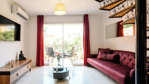 Een moderne woonkamer met een bank, een salontafel, een televisie en een balkon met rode gordijnen.