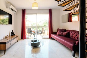 A modern living room with a sofa, a coffee table, a TV, and a balcony with red curtains. - Cristal 4 Apartment (Cannes)