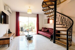A modern living room with a sofa, a coffee table, a TV, and a staircase with a decorative railing. - Cristal 4 Apartment (Cannes)