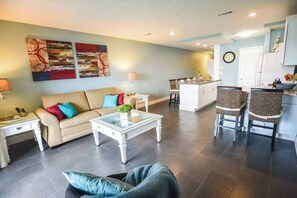 A living room with a sofa, coffee table, and chairs, a kitchen with a dining area, and artwork on the walls. - Steps to Beach, Zen balcony, Pier Park & more (Panama City Beach)