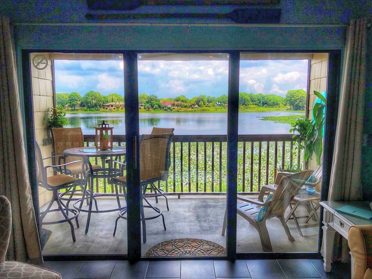 A room with a sliding glass door leading to a balcony with a view of a lake and greenery.