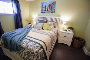 Ein Schlafzimmer mit einem Bett, Nachttischen, einer Lampe, einer Zimmerpflanze und einem Bild an der Wand.