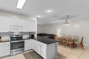 A modern kitchen with white cabinets, a built-in microwave, a stove, and a dining area with wooden chairs and a table. - The Rivalry House 10 Bedroom W/ Private Pool and Short Walk to Beach (Surfside Beach)