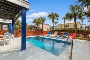 A swimming pool with lounge chairs, palm trees, and a wooden fence. - The Rivalry House 10 Bedroom W/ Private Pool and Short Walk to Beach (Surfside Beach)