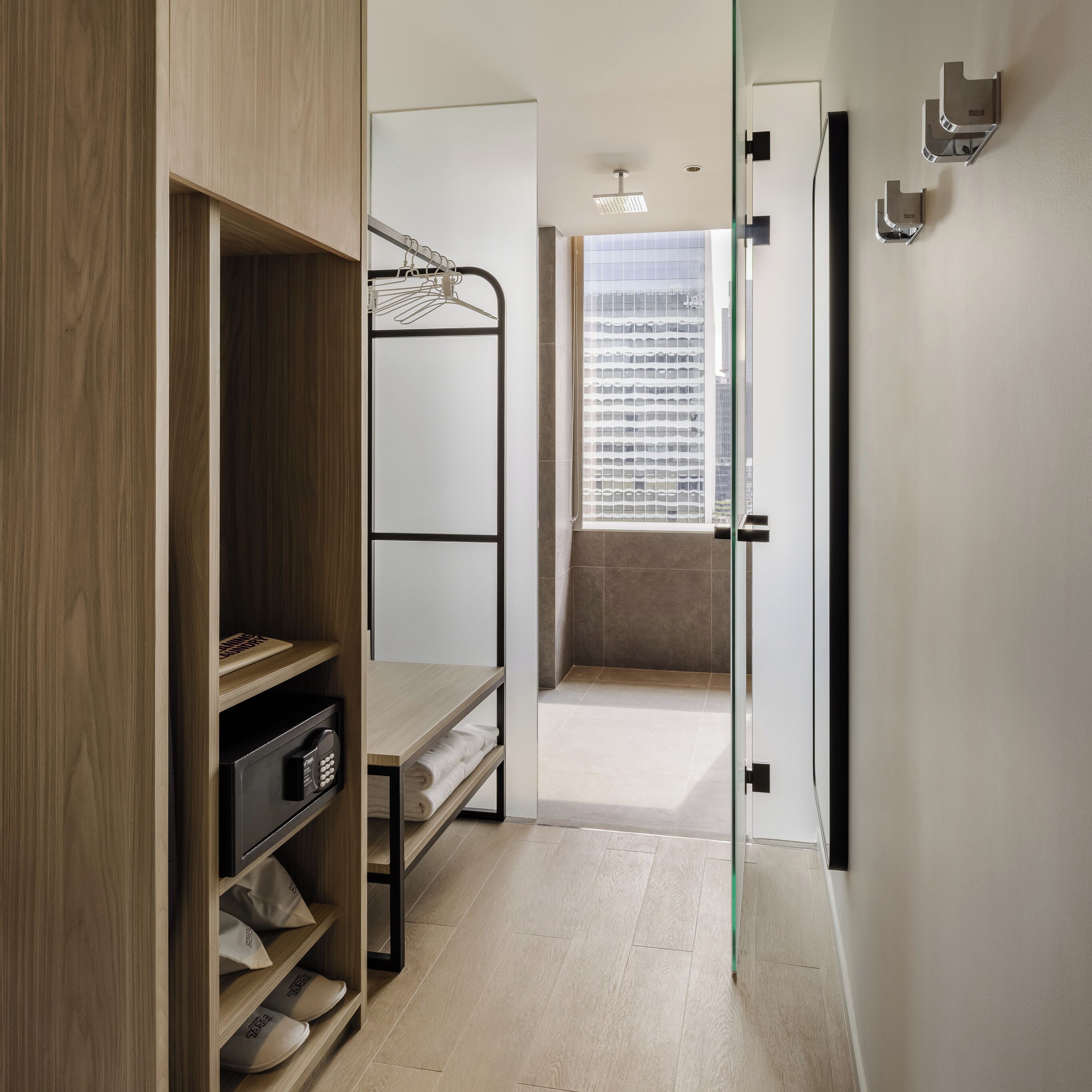 Une chambre d’hôtel moderne avec un lit superposé, une armoire et une vue sur le paysage urbain grâce à une grande fenêtre.