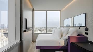 Een moderne hotelkamer met een groot raam, een bed, een bureau en een spiegel.