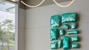 Un salon moderne avec un canapé beige, des coussins verts et un élément décoratif turquoise fixé au mur.