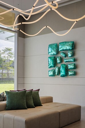 Una sala de estar moderna con un sofá color beige, cojines verdes y un adorno azul verdoso en la pared.