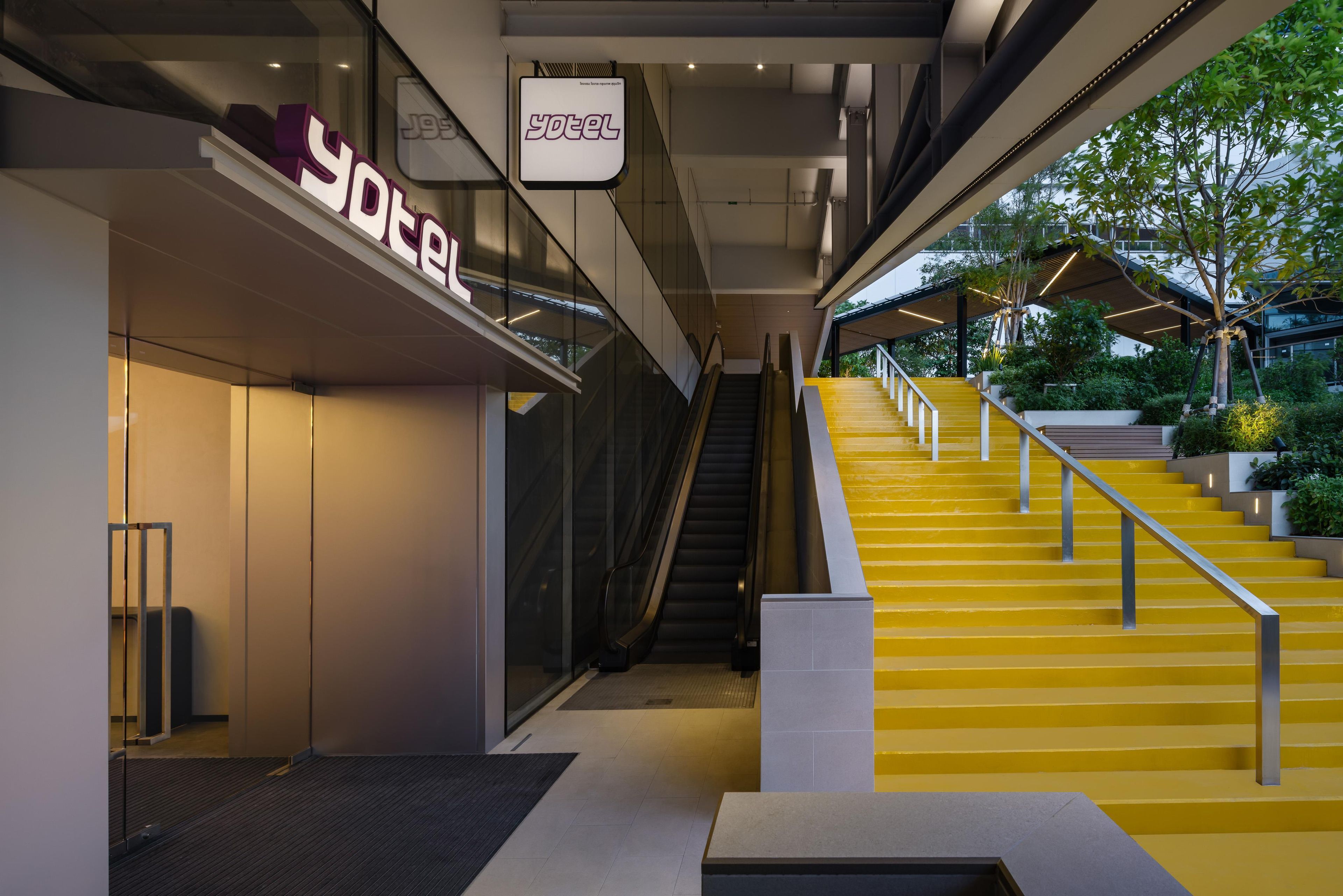 Un intérieur d’hôtel moderne avec un escalier menant à un espace extérieur, un comptoir d’accueil et une enseigne indiquant le nom de l’hôtel.