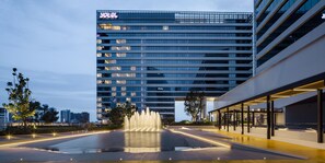 Een modern hotel met een opvallend 'HOTEL'-bord, een waterfontein en een goed verlicht buitengebied.