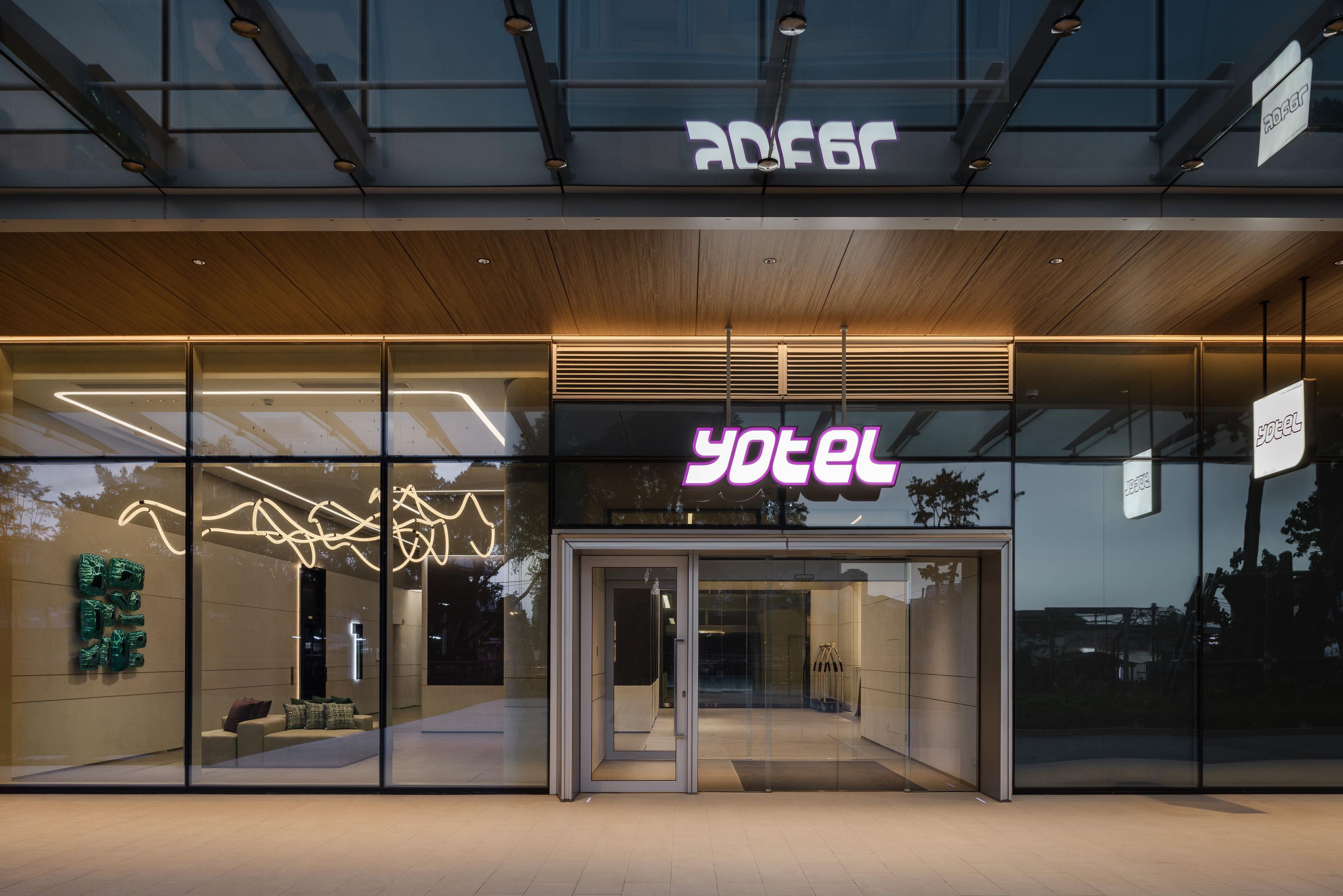 Ein moderner Hotel Eingang mit Glastüren und einem Neonlichtschild.