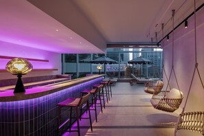 Een moderne bar met een toonbank, barstoelen, hangstoelen en uitzicht op de stad door grote ramen.