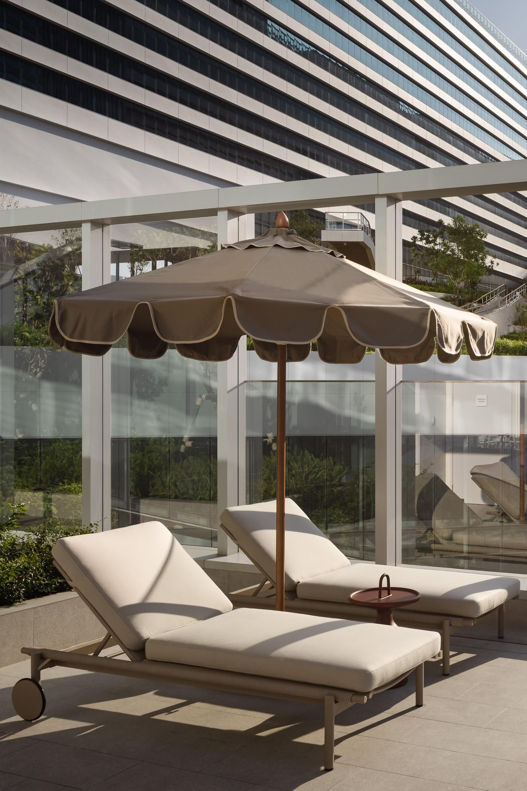 A modern outdoor lounge area with two sunbeds and a large umbrella.