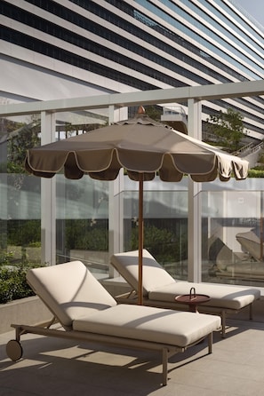 A modern outdoor lounge area with two sunbeds and a large umbrella. - YOTEL Bangkok Sukhumvit (Bangkok)