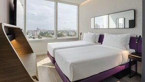Une chambre d’hôtel avec deux lits, une grande fenêtre, un bureau et une vue sur la ville.