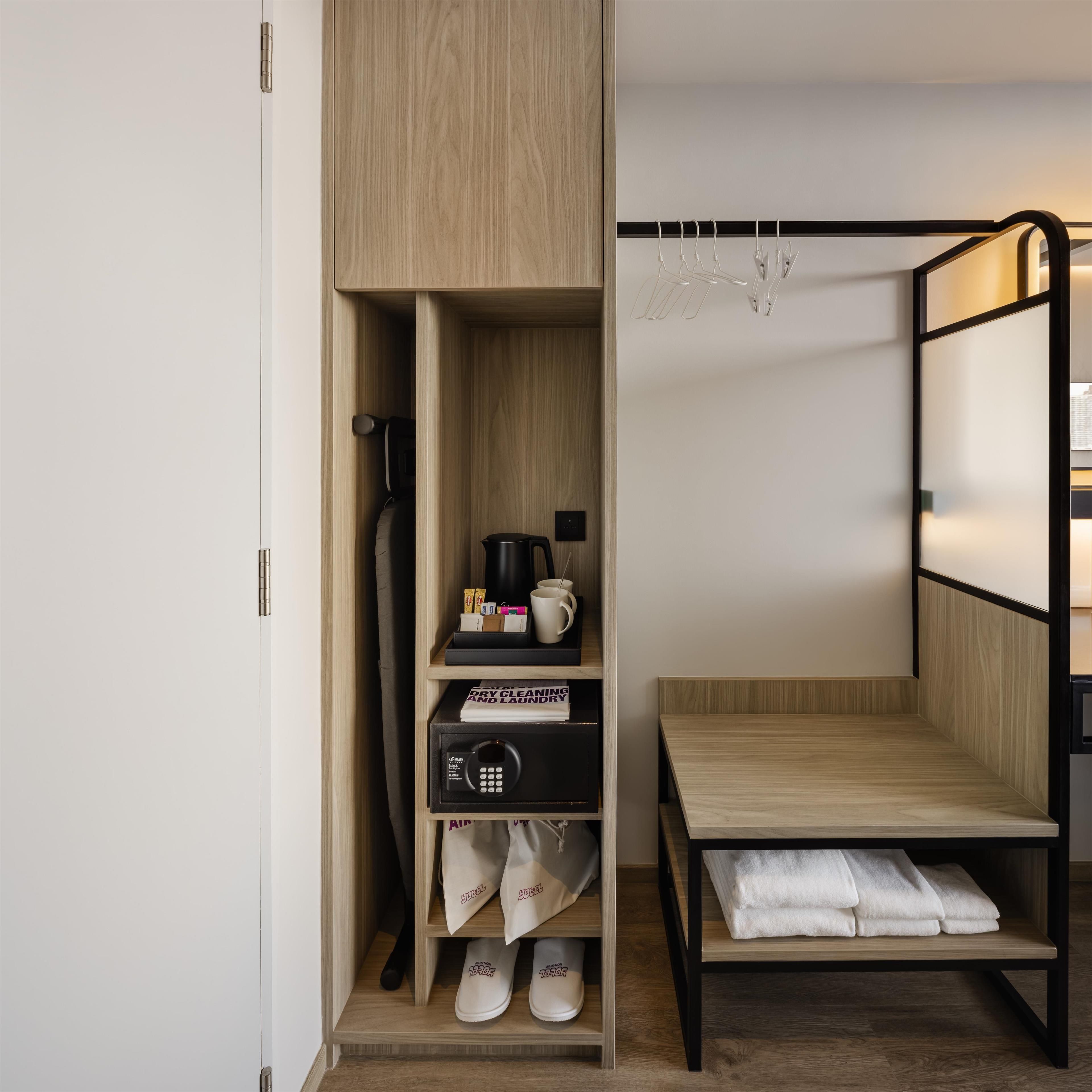 A compact room with a built-in wardrobe, a small seating area, and a drying rack.