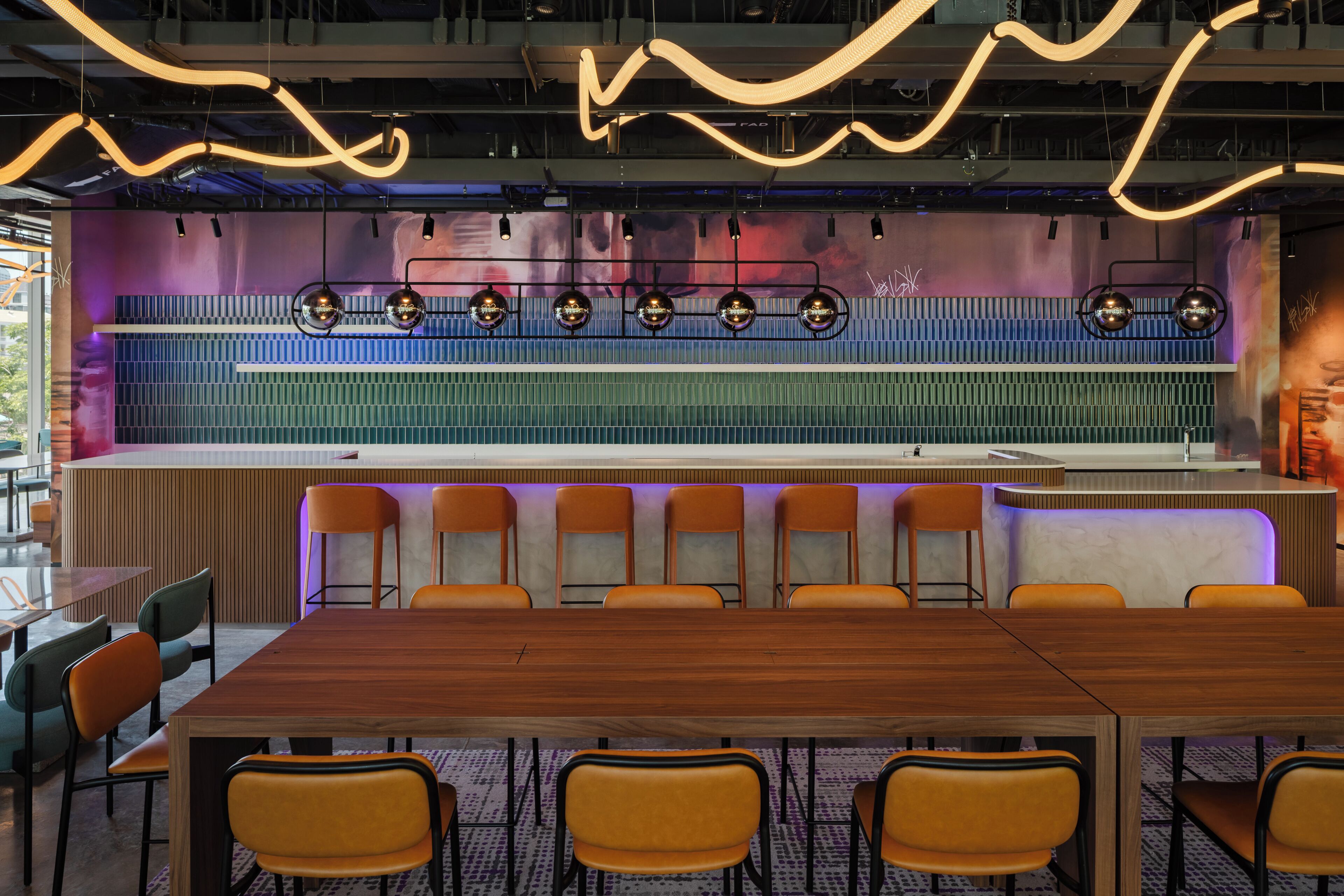 A conference room with a long table and multiple chairs, a modern light fixture, and a colorful wall with a grid pattern.