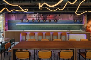 Un salón de conferencias con una larga mesa y varias sillas, una lámpara moderna, y una pared colorida con un diseño de cuadrícula.