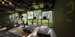 Een fitnessruimte met loopbanden, elliptische trainers en een digitale klok waarop 08:20 staat.