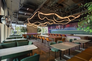 Een modern restaurantinterieur met hoge plafonds, zichtbare leidingwerk en diverse zithoeken, waaronder hoekbanken en losse tafels.