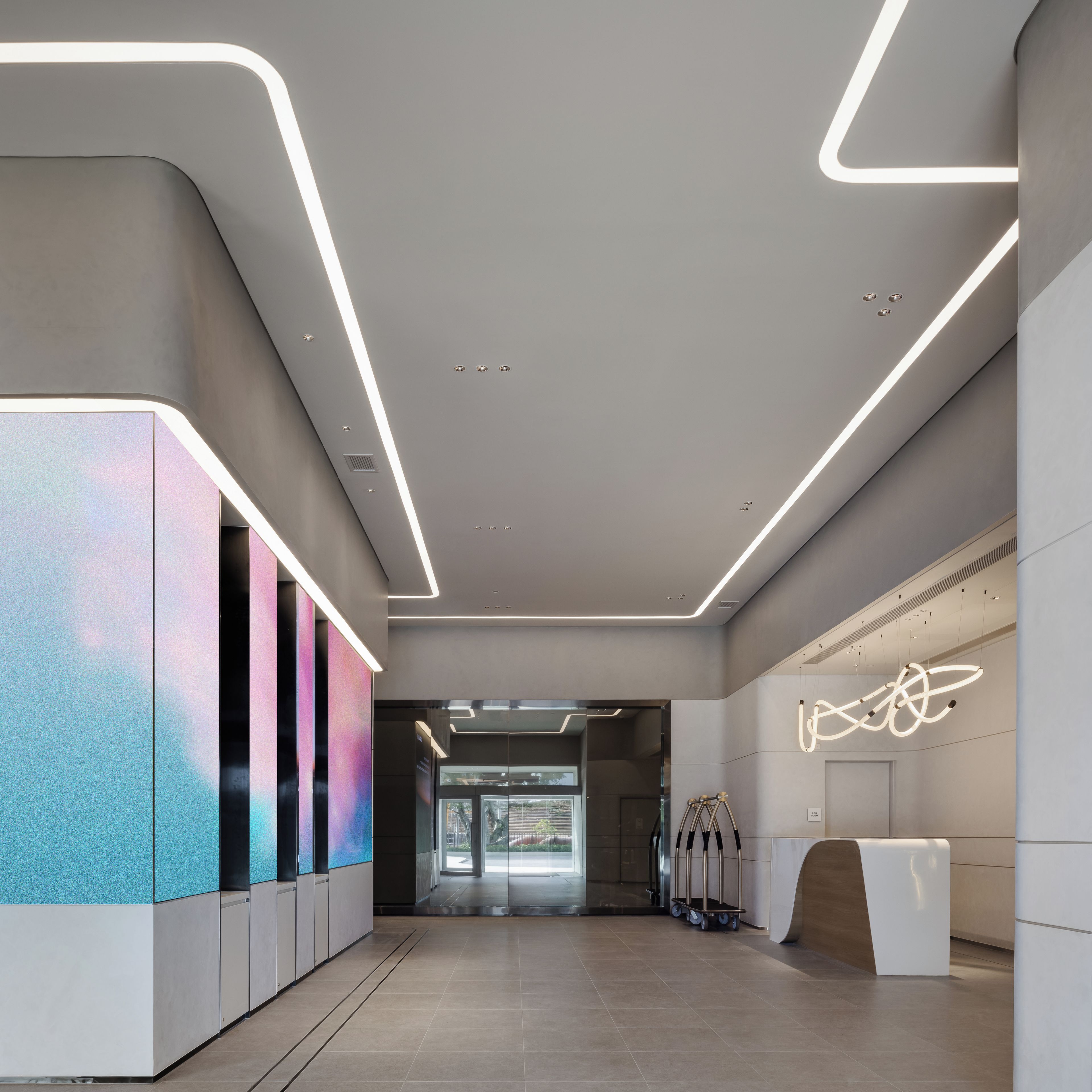 Un hall d’entrée moderne avec un comptoir d’accueil aux lignes courbes, un écran diffusant des œuvres d’art numériques et un design minimaliste.