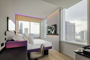 Een moderne hotelkamer met een bed, een bureau, een stoel, een televisie en uitzicht op de stad.