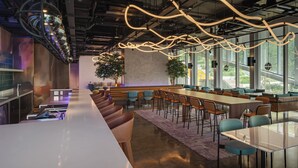 Un espace bar moderne doté d’un long comptoir, de sièges et de grandes fenêtres.