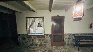 A room with a stone floor, a wooden door, a bench, and a hanging lantern.