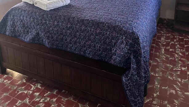 A bedroom with a wooden bed, white pillows, a blue quilt, and a window with curtains.