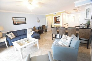 A living room with a sofa, coffee table, and a dining area with chairs and a table. - Beachfront Condo, Gulf View, Balcony, Beach Chairs, Heated Pool, Jacuzzis (Panama City)