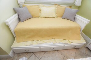 Ein Bett mit gelber Bettdecke und Kissen, einem weißen Kopfteil und einer kleinen weißen Kommode darunter.