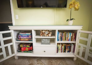A white entertainment unit with a flat-screen TV above, a small potted plant, and bookshelves filled with books. - Beachfront Condo, Gulf View, Balcony, Beach Chairs, Heated Pool, Jacuzzis (Panama City)