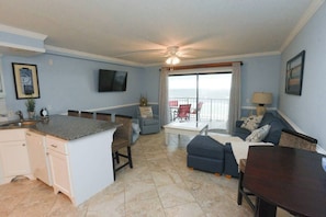 A living room with a sofa, a dining table, and a kitchen area with a counter and cabinets. - Beachfront Condo, Gulf View, Balcony, Beach Chairs, Heated Pool, Jacuzzis (Panama City)