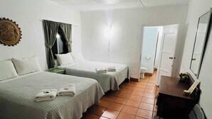 Une chambre d’hôtel avec deux lits, un bureau, une chaise, un miroir et une porte donnant sur une autre pièce.