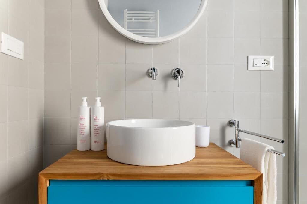 Un bagno con un lavandino bianco rotondo, due rubinetti, uno specchio e un portasacchi.