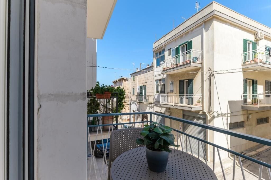 Ein Balkon mit einer Topfpflanze, einem runden Tisch und Blick auf angrenzende Gebäude.