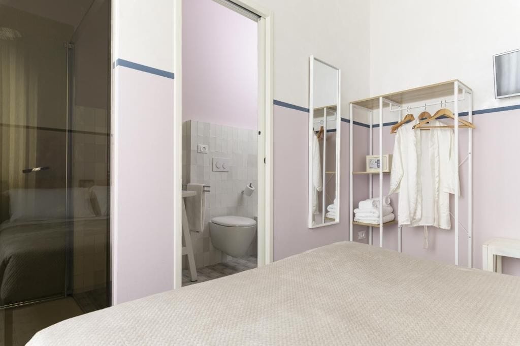 Ein Hotelzimmer mit Bett, Duschbereich, Toilette, Spiegel und Kleiderhaken.