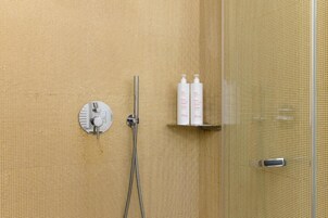 Een douchegedeelte met bedieningspaneel, douchekop en plank met toiletartikelen.